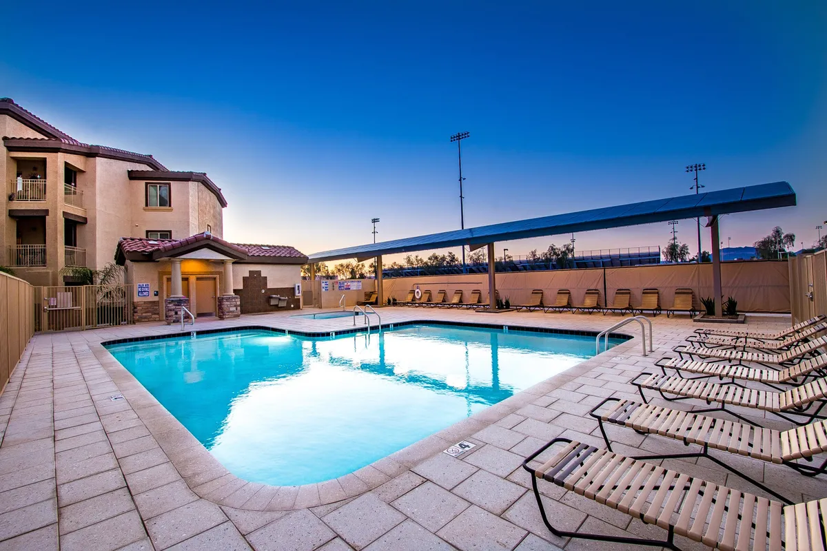 A serene view of the community swimming pool with inviting lounge chairs lined up along the water, set against the backdrop of the building facade. The calm water and well-kept surroundings evoke the tranquility and upscale feel of a resort.