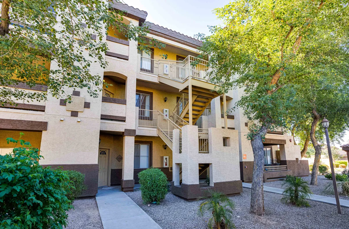 An exterior view featuring a staircase, entrance door, landscaped area, and windows. The scene is inviting and highlights both the residential character and the community feel of the property, with greenery offering a pleasant backdrop for walks or evening outings.