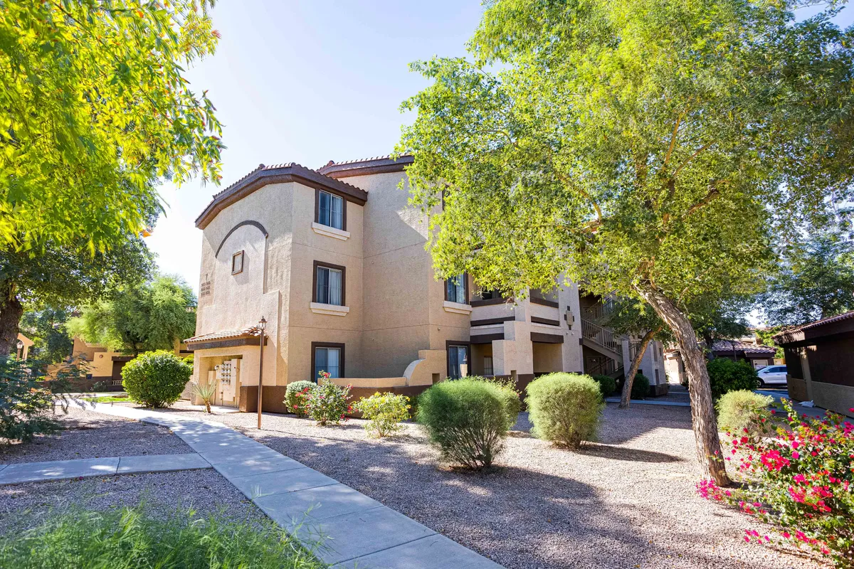 A beautifully landscaped garden lines a winding pathway, leading up to a welcoming building facade. The greenery and bright flowers create a peaceful, inviting ambiance, perfect for morning walks or evening strolls. The space suggests opportunities for outdoor relaxation and enjoying nature close to home.
