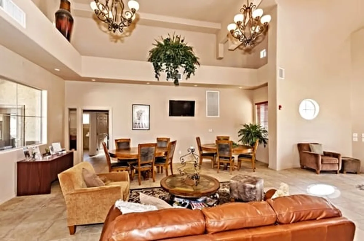 A spacious, open interior features a wooden dining table beneath a large chandelier, a comfortable leather sofa, and potted plants, all set in a well-lit, inviting space. The setup suggests a place where families can gather for meals, play games, and make memories together at home after exploring local attractions.