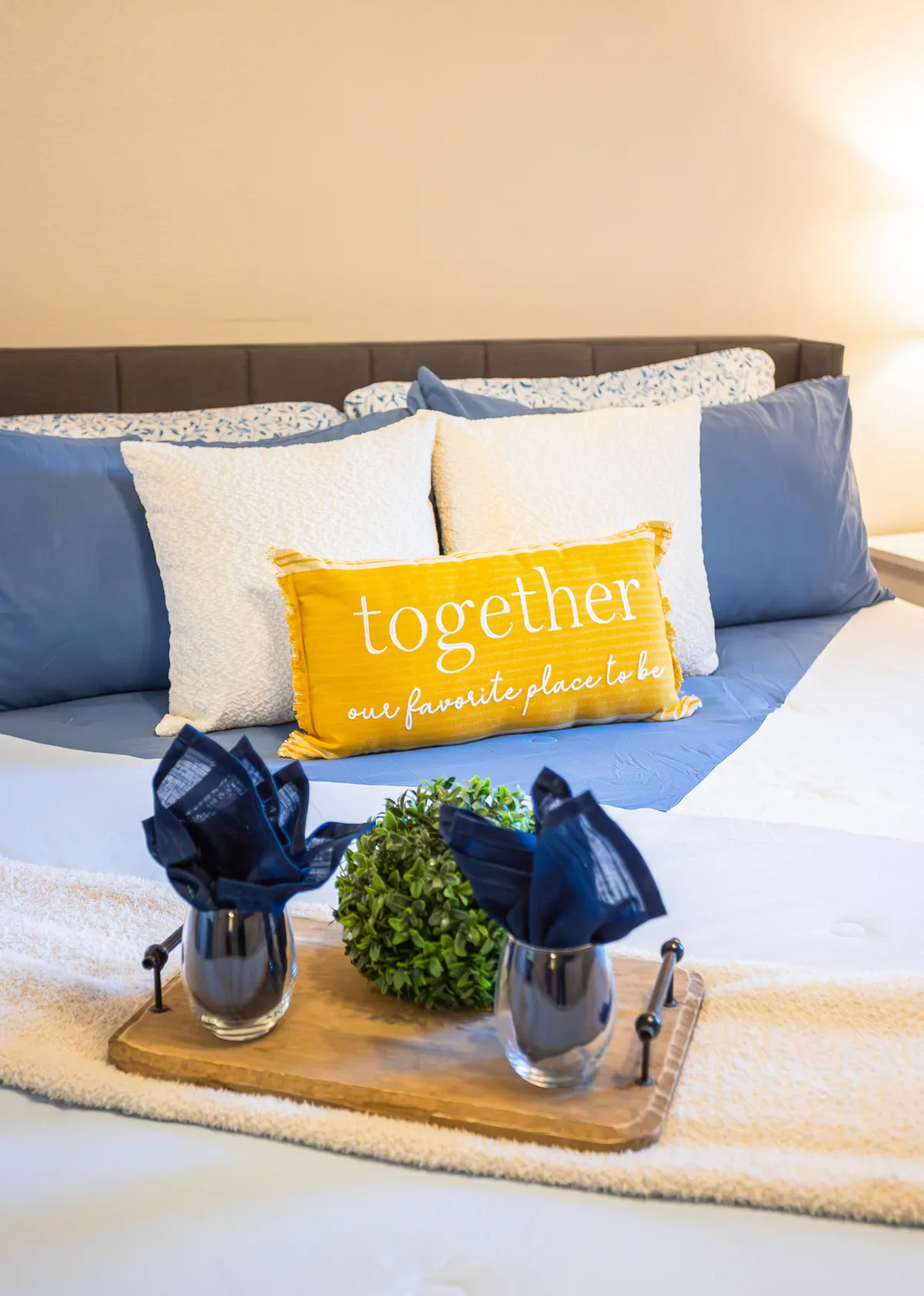 A cozy seating area adorned with a cheerful yellow pillow featuring text, complemented by blue and white patterned pillows and a decorative tray with greenery. The scene radiates warmth and encourages quiet relaxation, reading, or moments of togetherness.