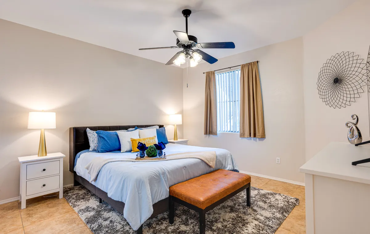 A serene and comfortable bedroom with a neatly made bed, stylish nightstands, a large window letting in natural light, decorative wall art, and a bench at the foot of the bed. The space feels airy and restful, perfect for unwinding.