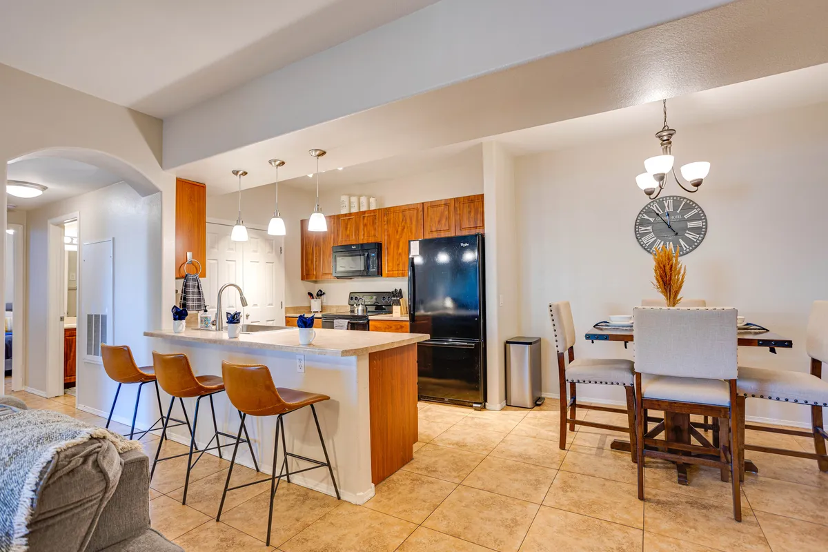 A bright, welcoming kitchen and dining area featuring a spacious island, stylish pendant lights, and a prominent wall clock. The setup invites group cooking, dining, and entertaining, with plenty of room for people to gather, share meals, and create memories together.