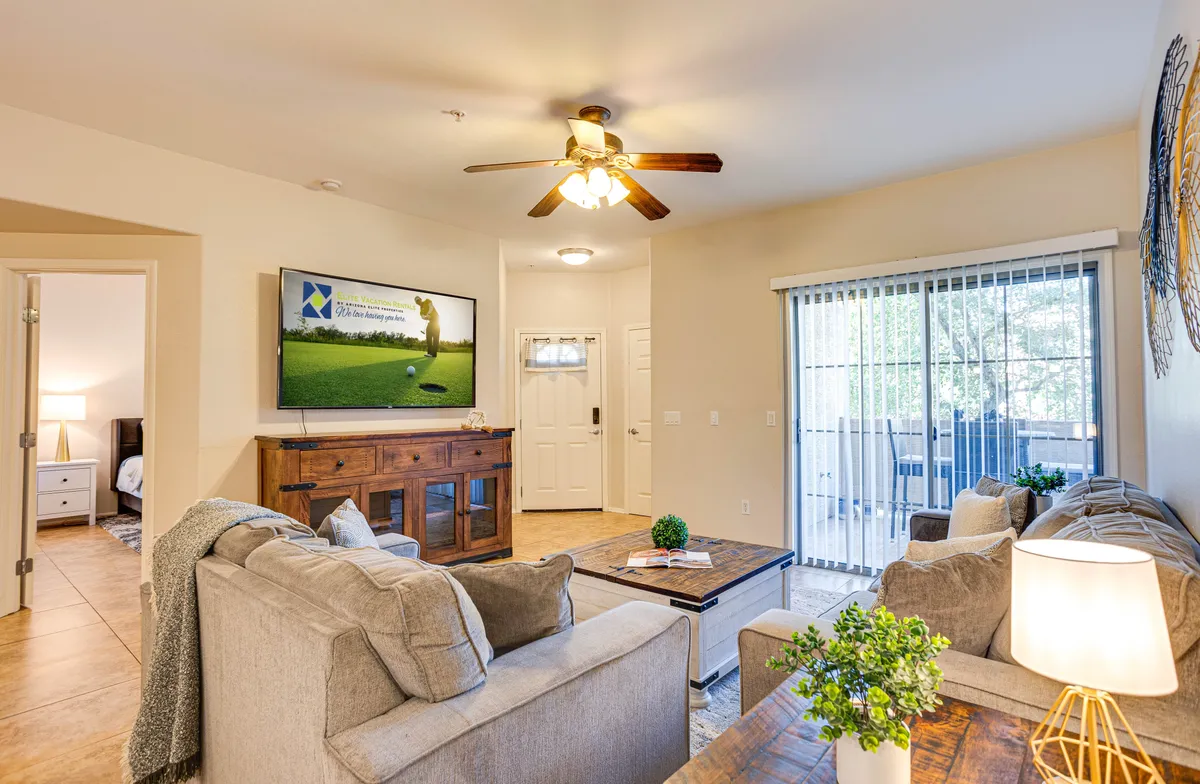 This cozy living room scene features a comfortable sofa, coffee table, television, and a sliding door leading to a patio. The natural light and view to the outdoors hint at relaxation after active days, with the space outfitted for unwinding or socializing.